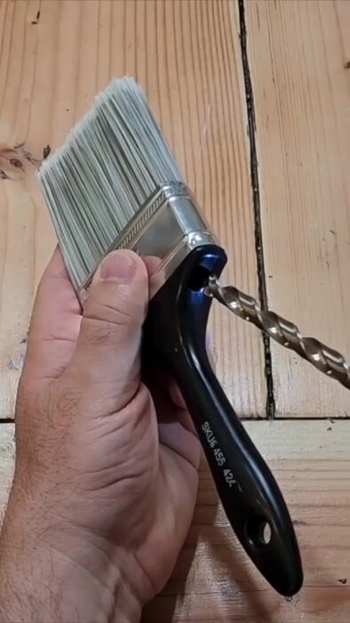 Hand håller en målarborste med en borrbit fastklämd i borstens handtag.