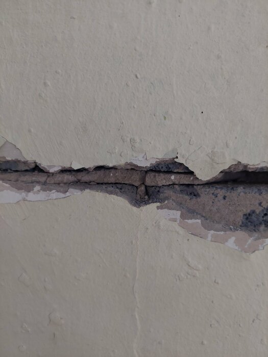 En skadad vägg med vittrande, poröst murblock synligt bakom sprucken och flagnande puts.