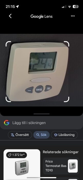 Digital termostat på väggen som visar en temperatur på 21.4 grader Celsius.