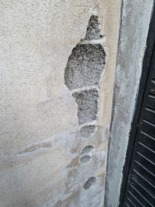 Skadad vägg med avfallen puts och exponerade, smulade lecakulor runt ett djupt hål.