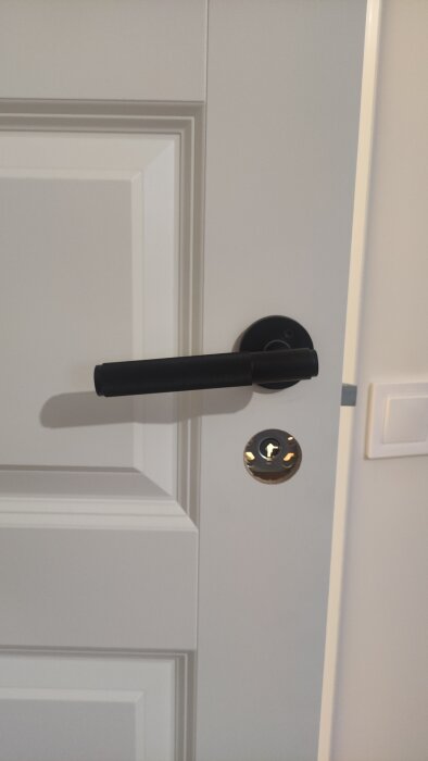 Ny monterat dörrhandtag på vit dörr sitter snett, med synlig låscylinder under.