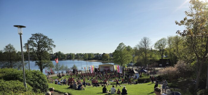 Panoramavy över Blodomloppet med deltagare och åskådare i en park vid en sjö under soliga förhållanden.