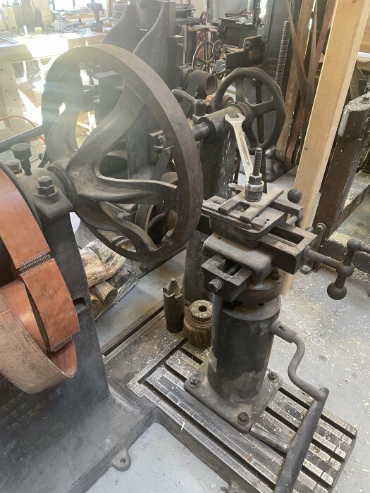 Äldre möbeltappmaskin i en snickarverkstad med stora hjul, spakar och verktyg, indikerar historisk hantverksteknik.
