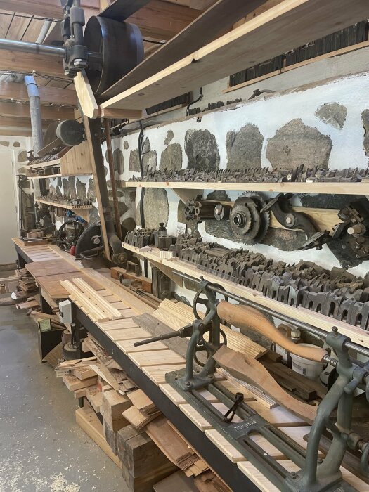 Verkstad med antik bandsåg och andra snickeriverktyg, träbitar ordnade på arbetsbänkar.