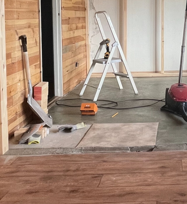 Renoveringsarbete med verktyg och en stege i ett rum där gammalt golv möter ny betongyta som ska spacklas.