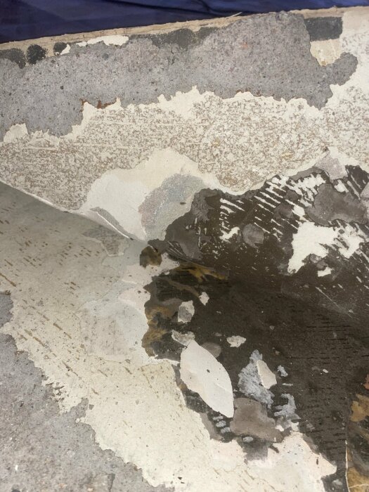 Delvis bortriven plastmatta i hörnet av ett rum som visar lager av golvmaterial, eventuellt innehållande asbest.