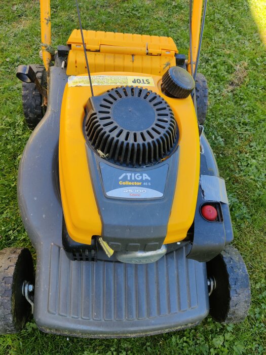 Gul och grå gräsklippare av märket Stiga med RS 100 OHV-motor som står på gräsmatta.