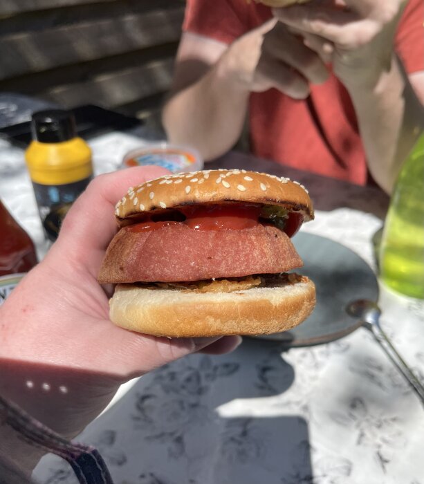 Hand håller en parisare med ketchup och rostad lök mellan bröd utomhus.