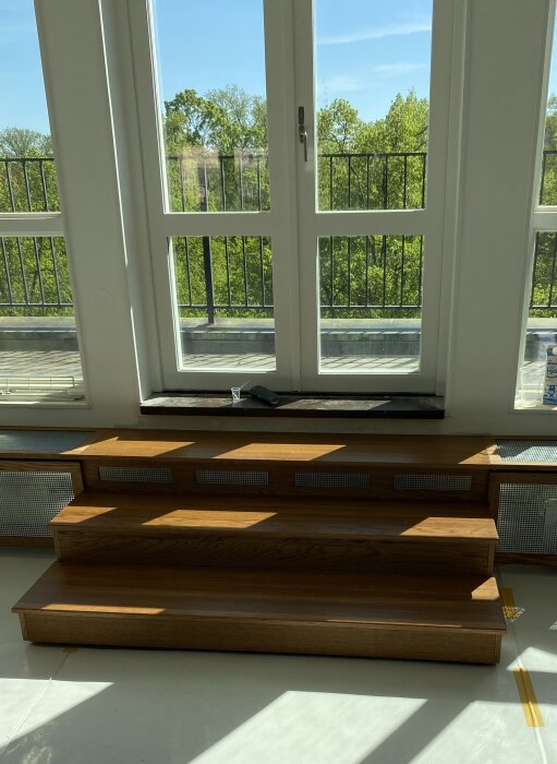 Nyinstallerade trätrappsteg med elementskydd integrerat i interiör vid ett soligt fönster.