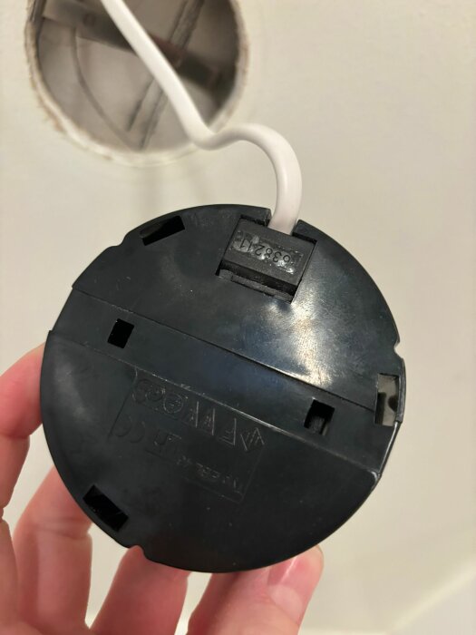 Hand håller en svart spotlightfot där ett vitt kabel sticker ut, visar fram och baksida.