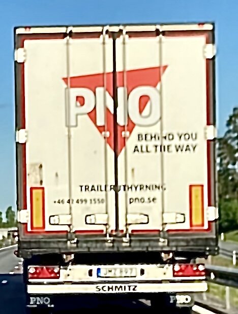 Lastbilsbak med texten "PNO - BEHIND YOU ALL THE WAY" på motorvägen.