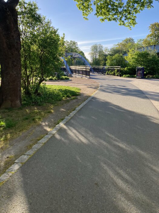 Solbelyst stadsmiljö med en fotgängarbro i bakgrunden och asfalterade gångvägar i förgrunden.