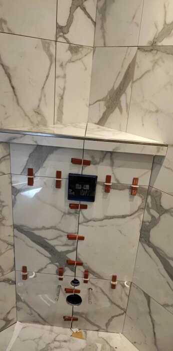 Nymonterade marmorerade kakelplattor med mätkors och en våtuttag låda under installation.