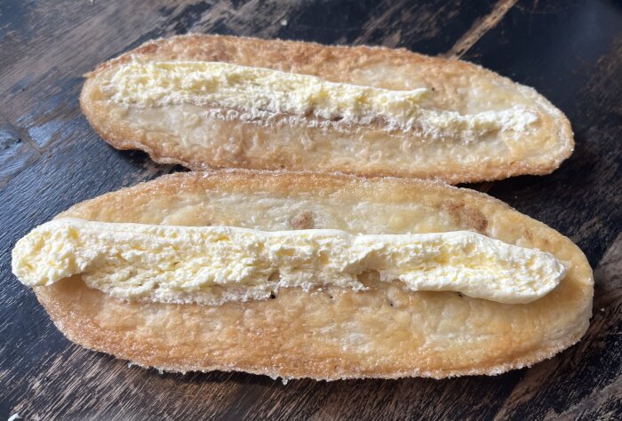 Två rostade brödhalvor med smält smör ovanpå på en mörk träbakgrund.