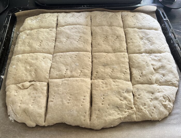 Hemgjort bröd på bakplåt före gräddning, indelat i fyrkanter och naggat, redo för ugnen.