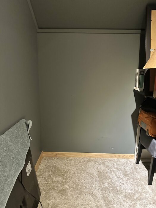 Vägg i rum med plats för planerad dold dörr till kattvind, delar av möbler syns.