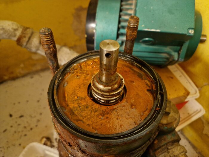 Rostig pumpdel med en metallaxel, täckt av orange rostavlagringar vid öppning av pumpens locket.