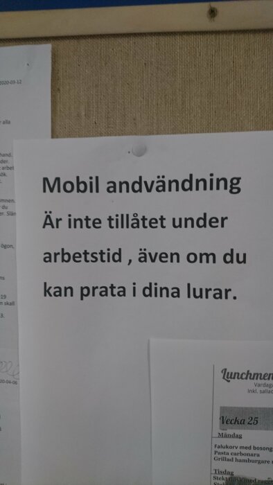 Anslag med texten "Mobil användning är inte tillåtet under arbetstid, även om du kan prata i dina lurar" på anslagstavla.