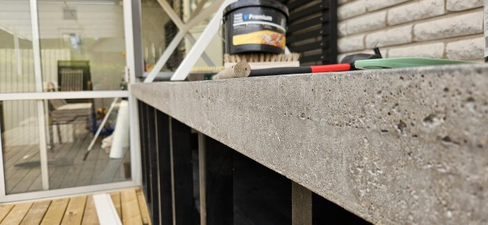 Gjuten betongbänkskiva på altan med synliga gropar och ojämnheter längs kanten, i behov av reparation.
