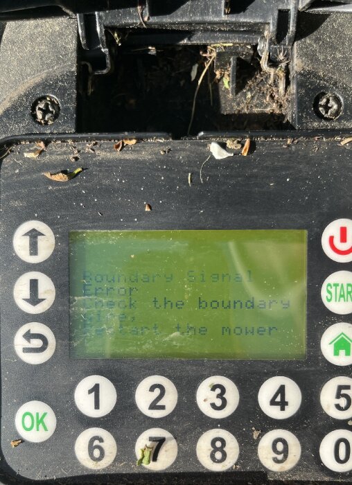 Skärmbild på en gräsklipparpanel som visar felkod 'Boundary Signal Error', smutsigt tangentbord under.