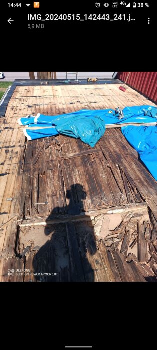 Skadat trä i takkonstruktion med tydlig vattenskada och fukt, och rivna bitar, över kök med oskadad altan i bakgrunden.