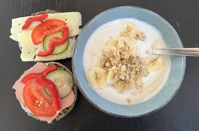 Frukost med yoghurt, banan och müsli samt mackor med ost, tomat och paprika.