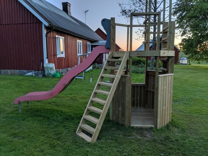 Hembyggd lekställning i trä med rutschkana, 10 trappsteg, bakgården av ett rött hus.