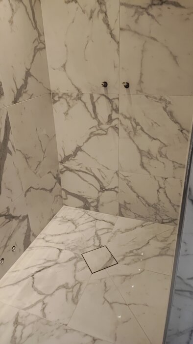 Nyfogat badrum med marmorerade kakelväggar och golv, skruvhål för spolknappen synliga.