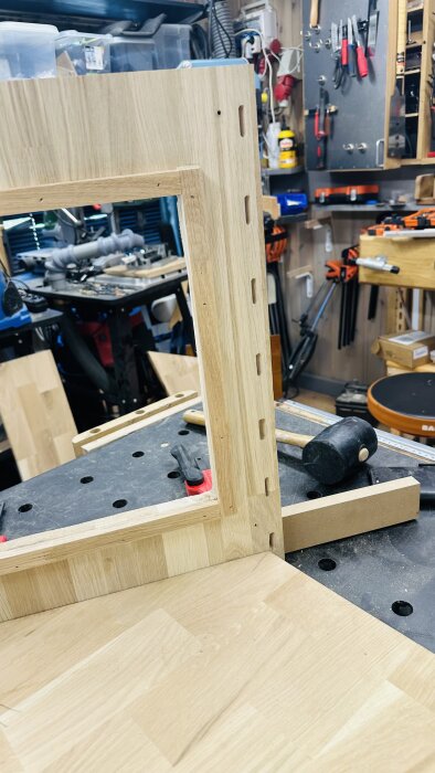 Ej monterad skåpsram i trä på ett arbetsbord i verkstad med verktyg i bakgrunden.