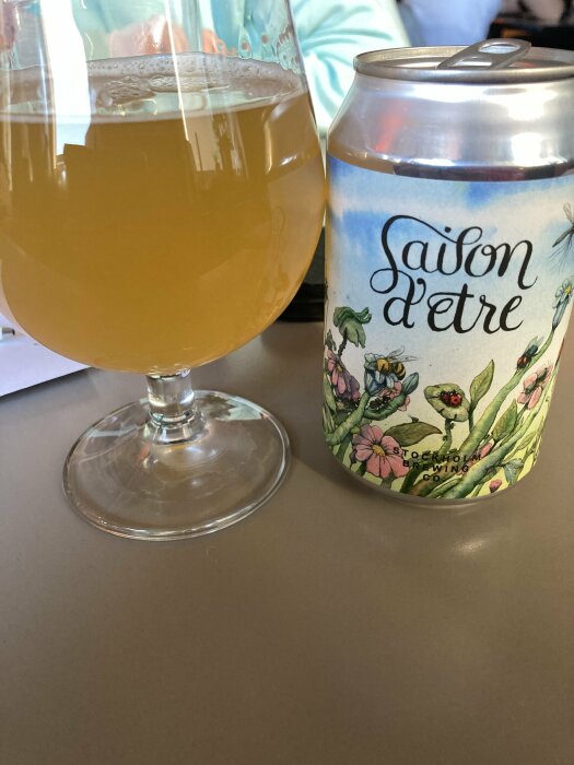 Ett glas med grumlig öl och en burk öl märkt 'Saison d'être' från Stockholm Brewing Co. på ett bord.