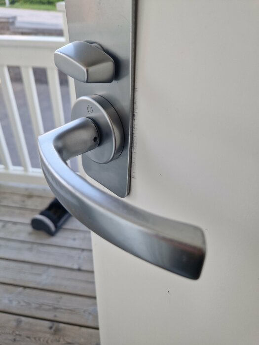 Närbild av ett dörrhandtag av metall monterat på en vit dörr, utan synliga skruvar eller monteringsdetaljer.
