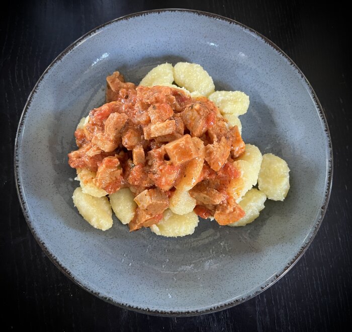 Gnocchi med tomatsås och köttbitar av porchetta serveras på en grå tallrik.