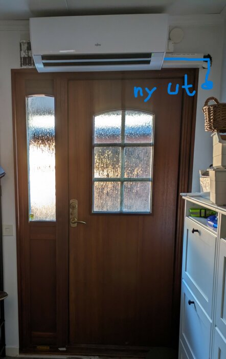 Luft-luftvärmepump installerad ovanför en brun dörr, med notering om att dra om kondensslangen.