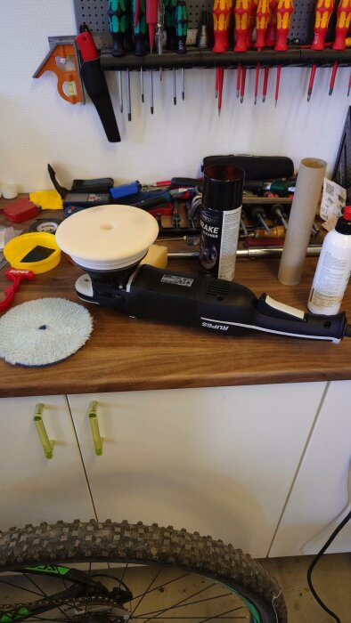 Polermaskin med vit poleringsrondell på ett arbetsbord med bilvårdsprodukter och verktyg i bakgrunden.