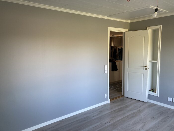 Nästan färdigt tomt sovrum med gråa väggar, golv i laminat, och en öppen dörr till en klädkammare.