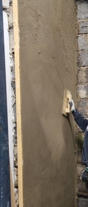 Person som använder en träbräda för att jämna till våt murbruk på en vägg.