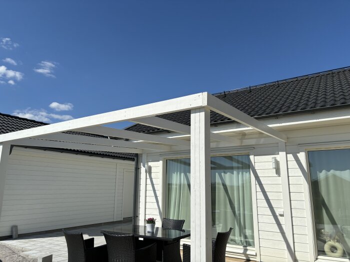 Vit träpergola (3,6x3,6 m) utan markis vid ett hus med uteservering och blå himmel.