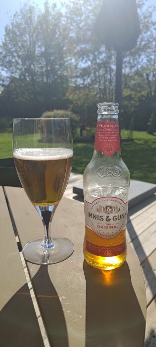 Öl i glas och Innis & Gunn-flaska på ett utomhusbord i solsken.