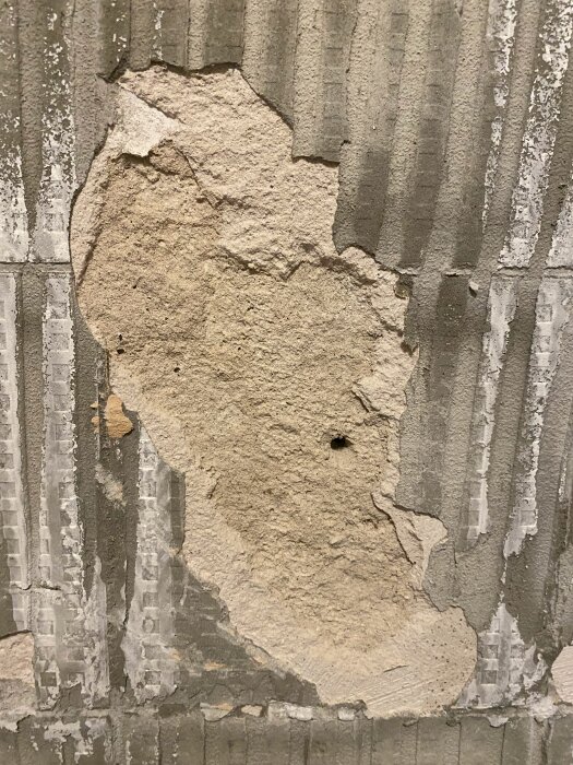 Riven vägg med gammal puts och rester av kakelfix, synlig skadad och porös struktur utan tätskikt.