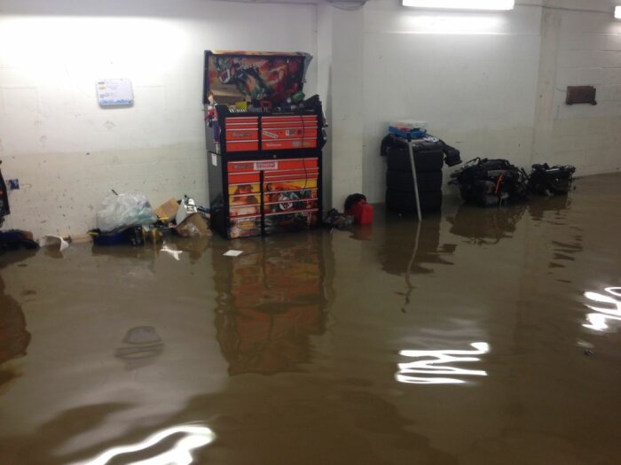 Översvämmat garage med verktygsskåp och föremål som är delvis nedsänkta i vatten.