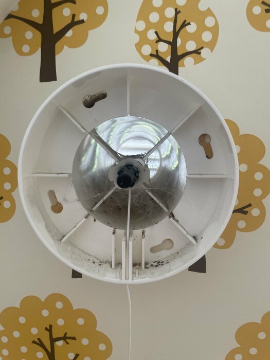 Framifrån-bild av en öppen Fresh-ventil med synlig plastkanal och ventilationsgaller på en vägg med träd-mönstrad tapet.