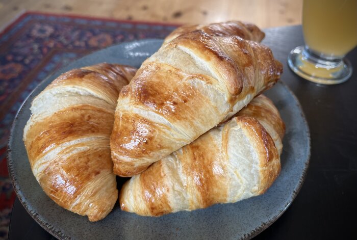 Nygräddade croissanter på en tallrik med ett glas äppeljuice i bakgrunden.