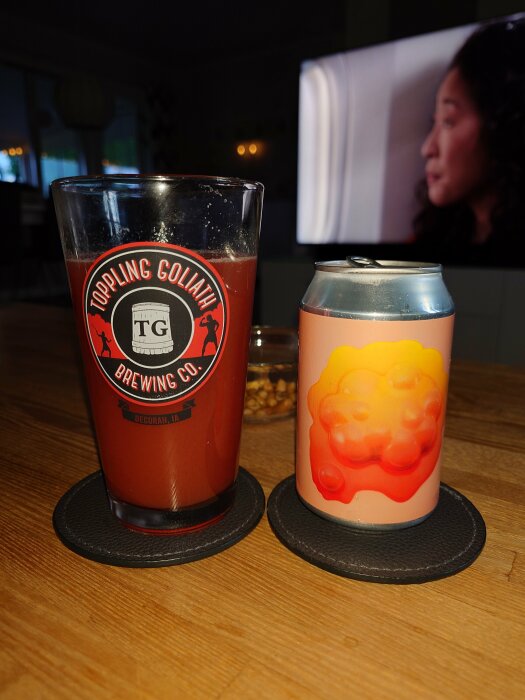 Ölglas med logotyp och burk av Omnipollo öl på träbord med en TV i bakgrunden.