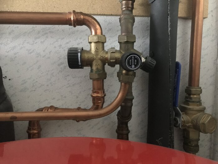 Röranslutningar och ventiler nära ett rött expansionskärl inom VVS-installation.