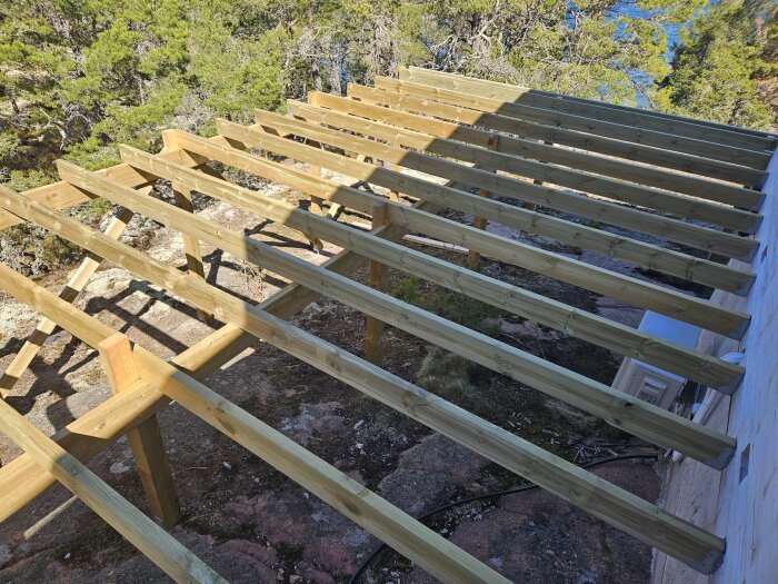 Delvis uppbyggt regelverk för altan med bärregler och skruvregler i trä på 2 meters avstånd, monterat intill husvägg.