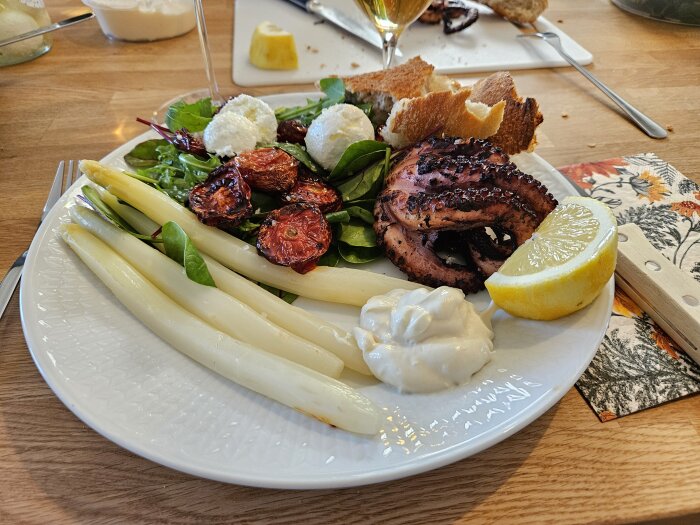 Grillad bläckfisk med sparris, tomat, sallad, mozzarella, citron och sås på en tallrik.