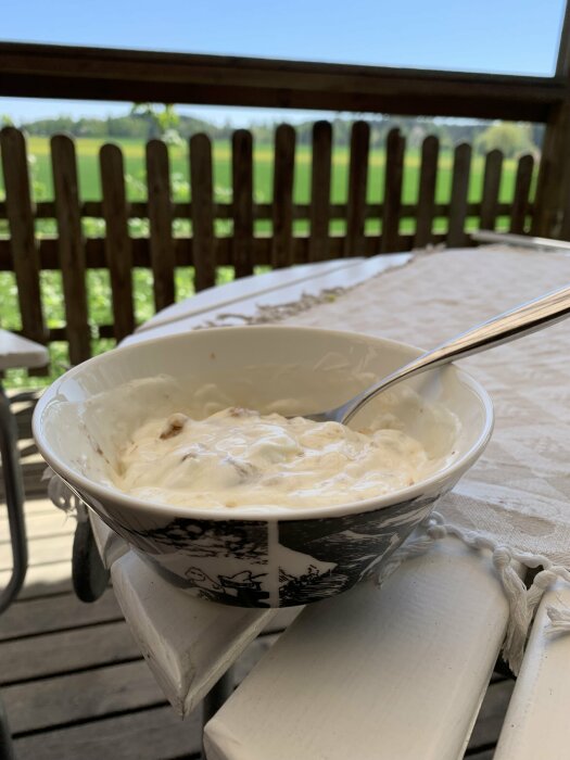 En skål med turkisk yoghurt, valnötter och honung på ett bord med utsikt över ett staket.