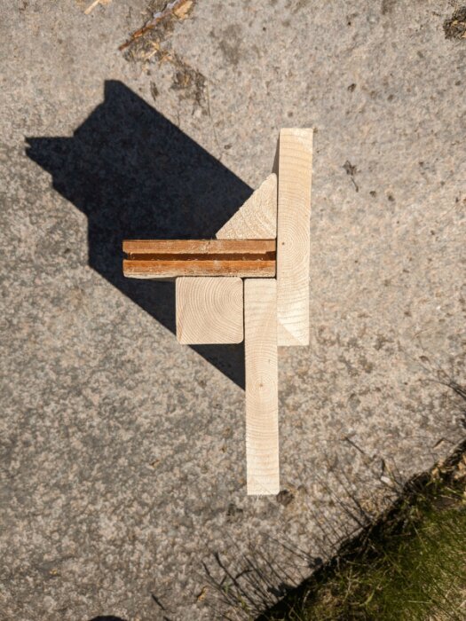 Mock-up av träkonstruktion löst placerad på marken, bestående av en vertikal och en horisontell träbit.