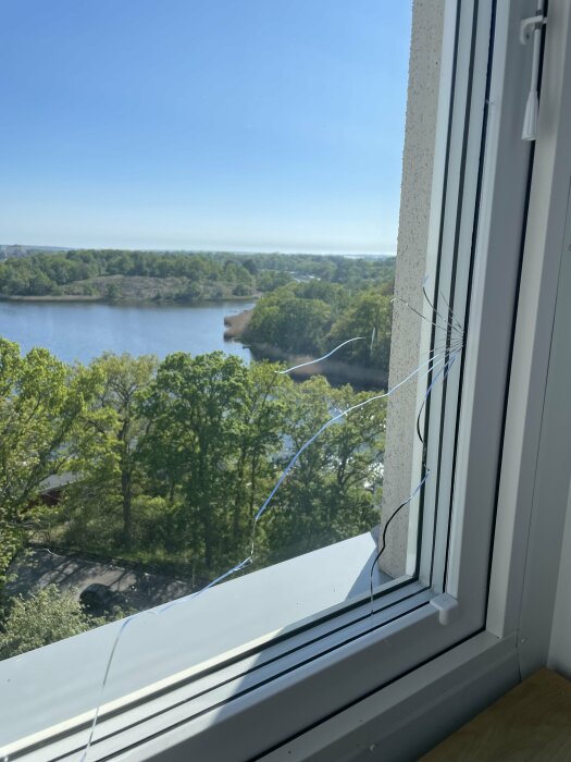 Sprucket inre glas på ett fönster med utsikt över sjö och träd, möjlig värmespricka från användning av portabel AC.