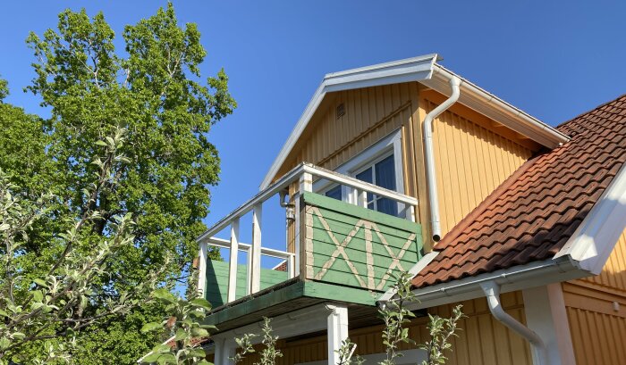 Halvfärdig rivning av en grönmålad balkong på ett gult trähus med blå himmel i bakgrunden.